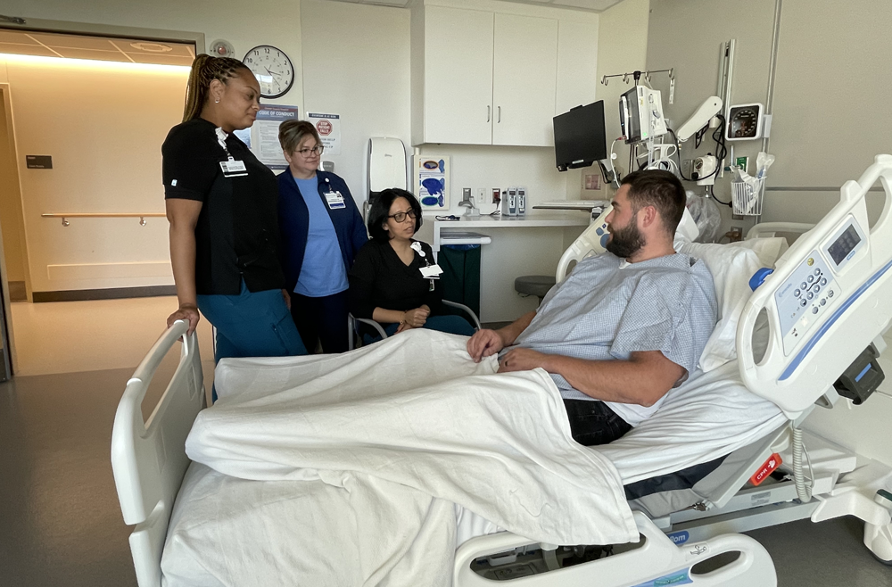 A patient is in a hospital bed, conversing with three healthcare professionals.